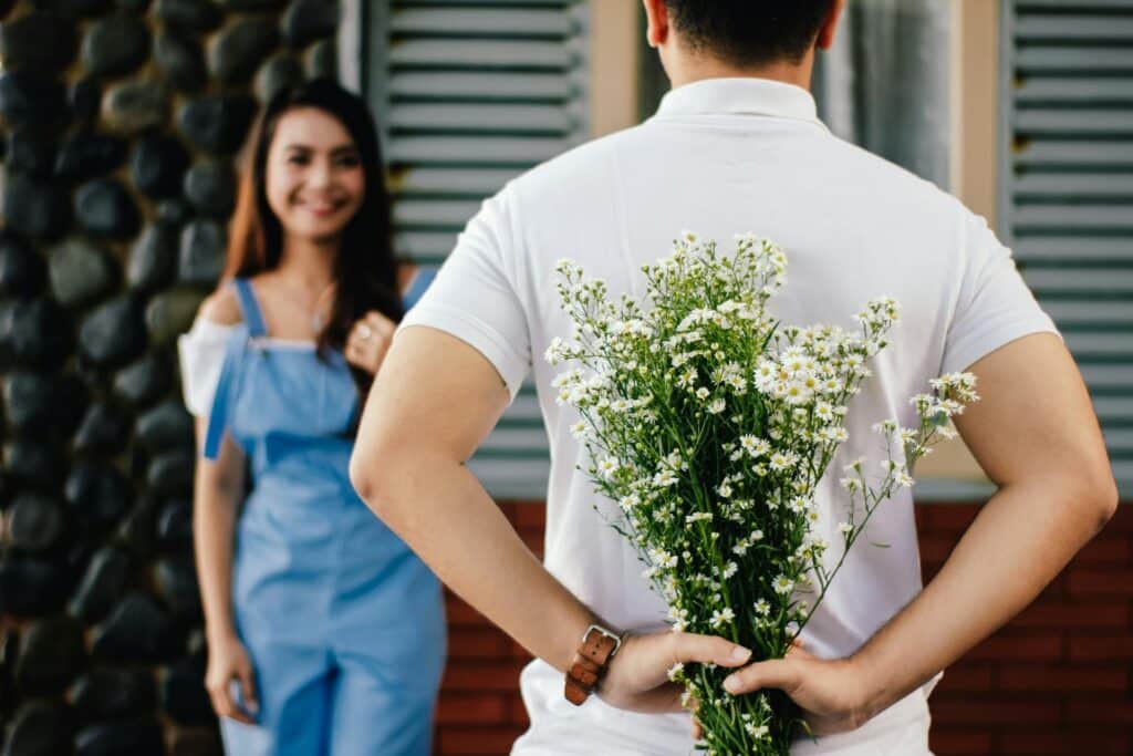 back-shot-of-man-holding-babys-breath-flowers-behind-him-with-woman-in-front-of-him