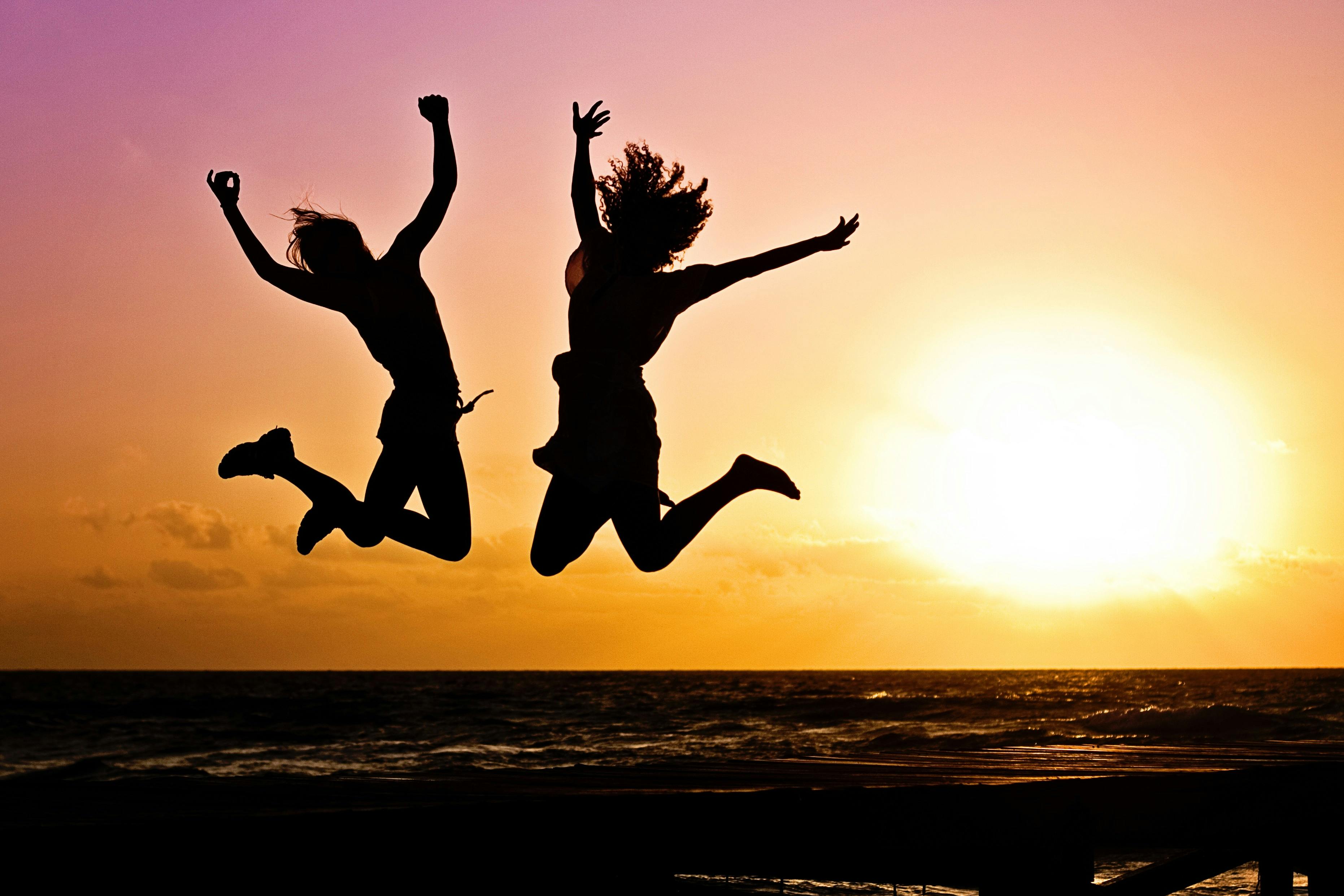 Two people jumping triumphantly up at sunset