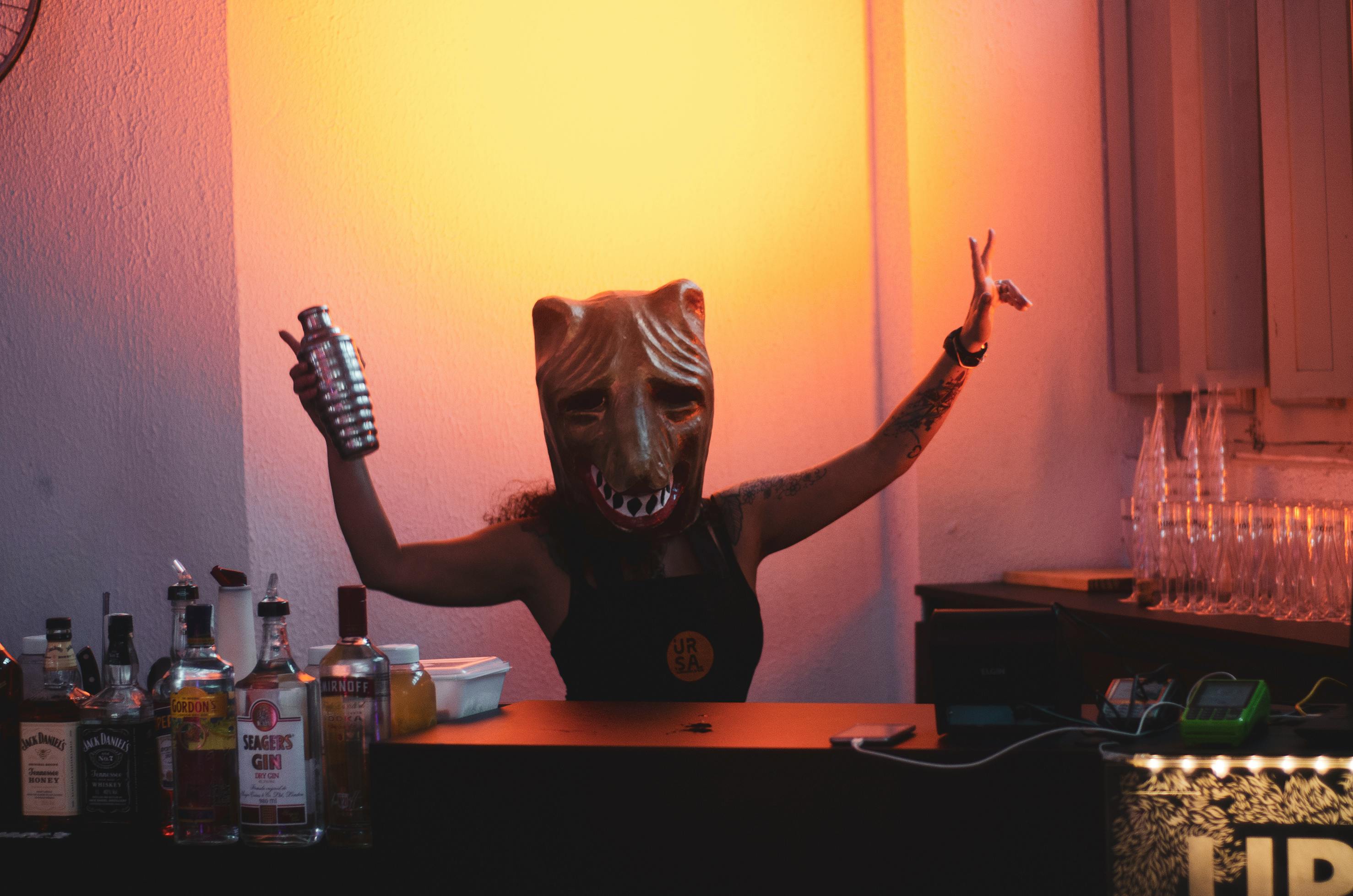 A person posing in a mask, holding a drink