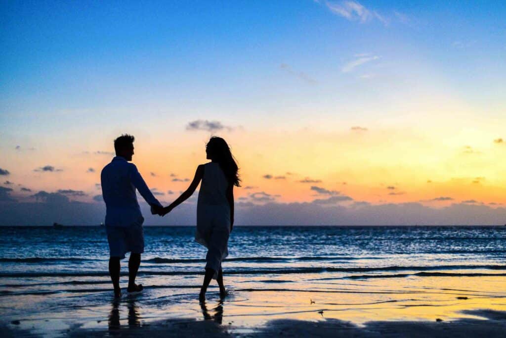 silhouette-of-man-and-woman-holding-hands-while-walking-on-the-beach-during-sunset