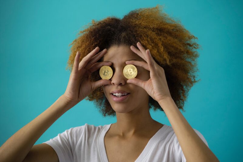 woman holding up two golden coins to her eyes against blue background