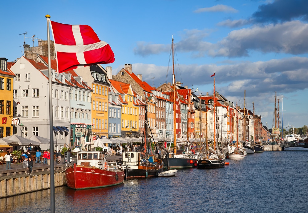 the Denmark flag flying over a river next to boats and traditional Danish buildings