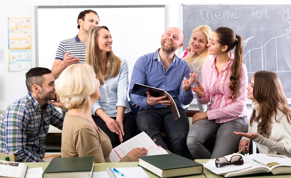 Charming language teacher is telling interesting stories to his attentive students during a break in a classroom