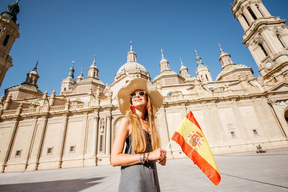 Woman-tourist-with-spanish-flag-in-front-of-the-cathedral-in-Zaragoza-city-Spain