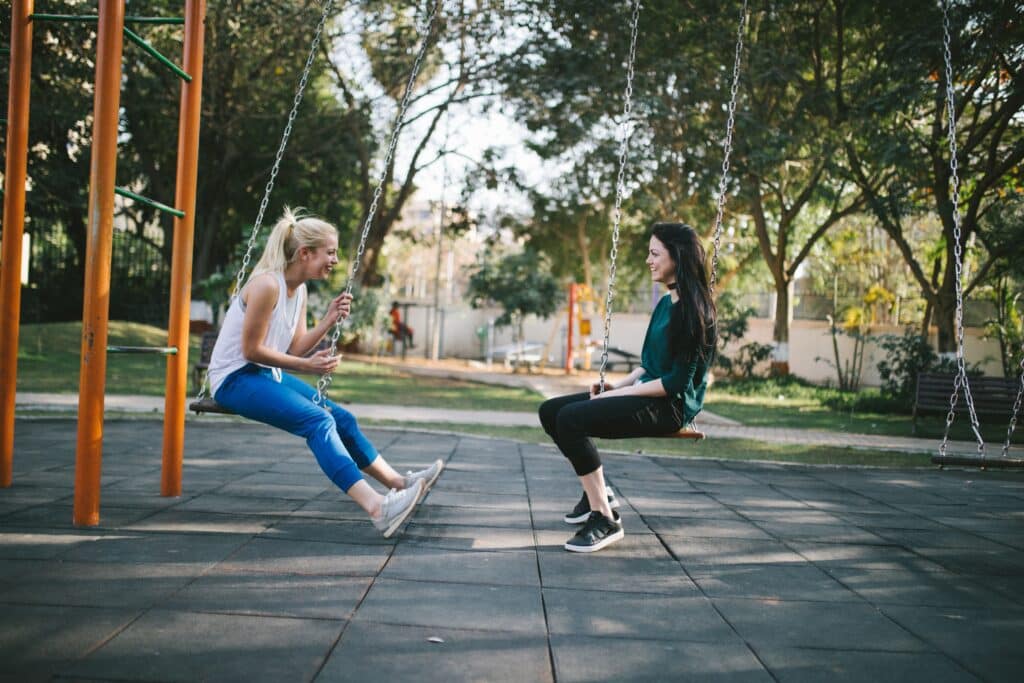 Two women talking while seated on swings