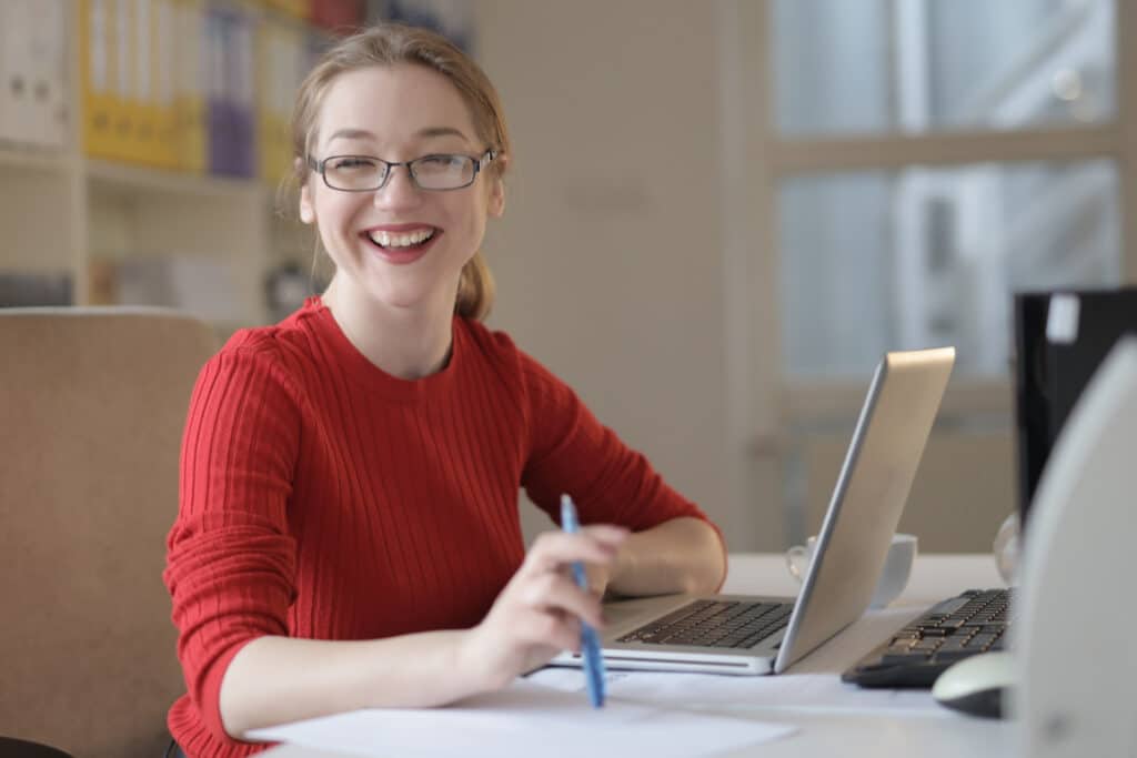 Person in a red shirt smiling next to laptop