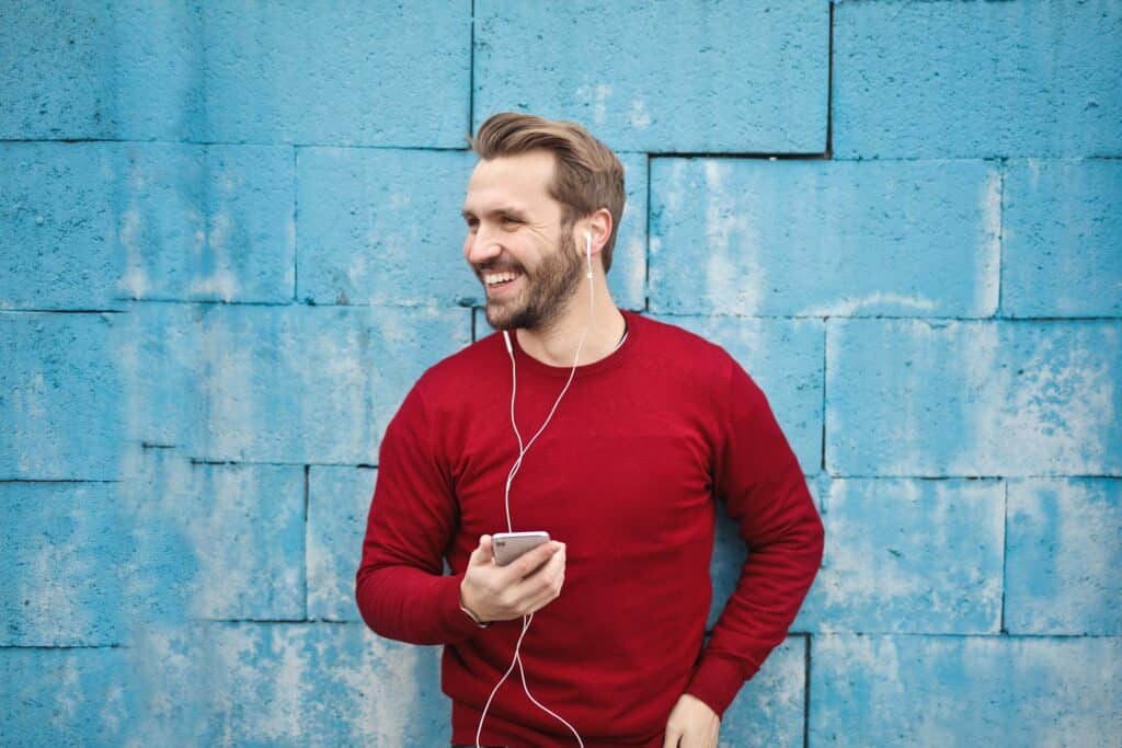 smiling-man-listening-to-device-standing-in-front-of-a-blue-wall