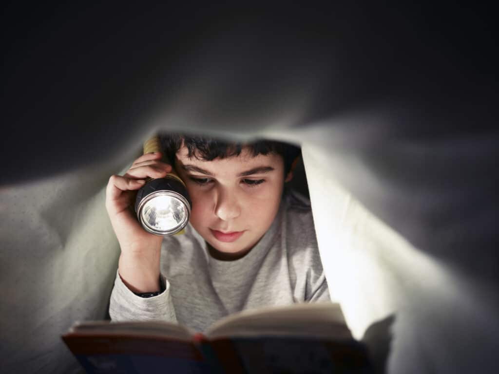 boy reading book with flashlight
