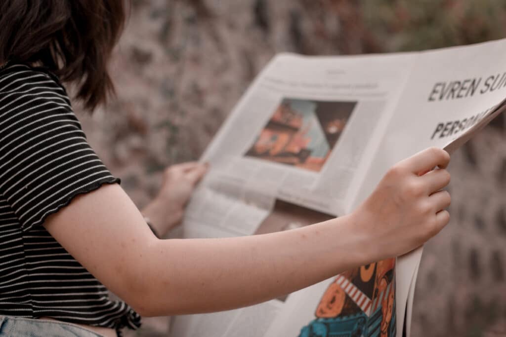 Person in stripy t-shirt reading a newspaper