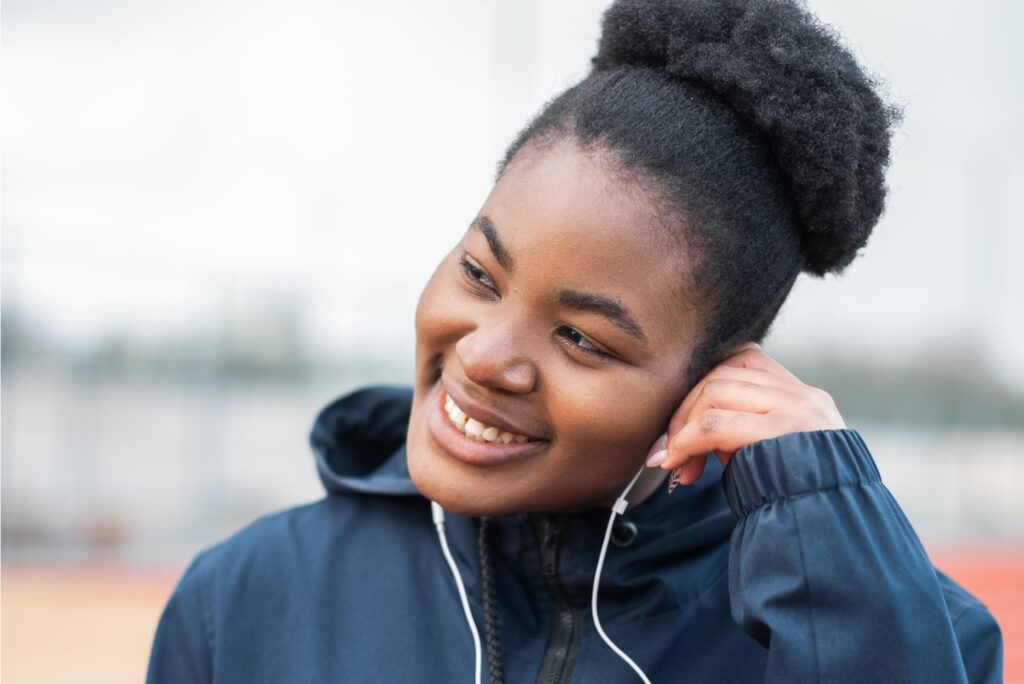 woman-of-africa-descent-smiling-as-she-presses-her-left-white-earphone-to-her-ear