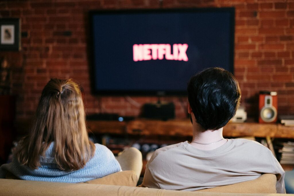 back-shot-of-couple-sitting-in-front-of-tv-screen-with-the-netflix-logo-on-it